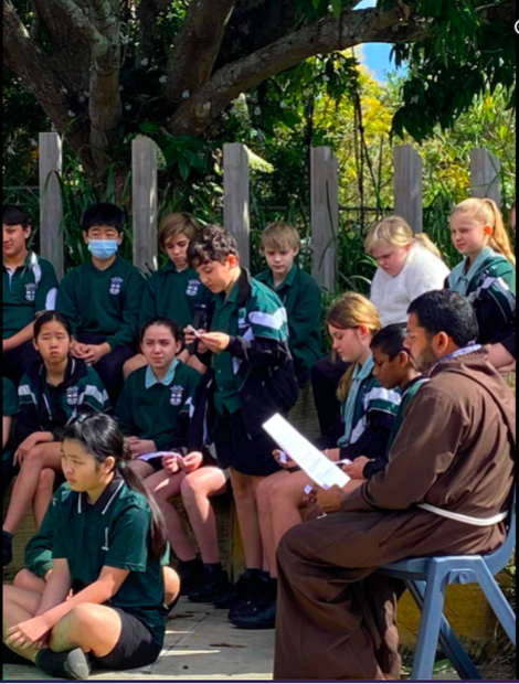 Students gathered outdoors with staff for a faith reflection, highlighting spiritual formation, listening and community worship